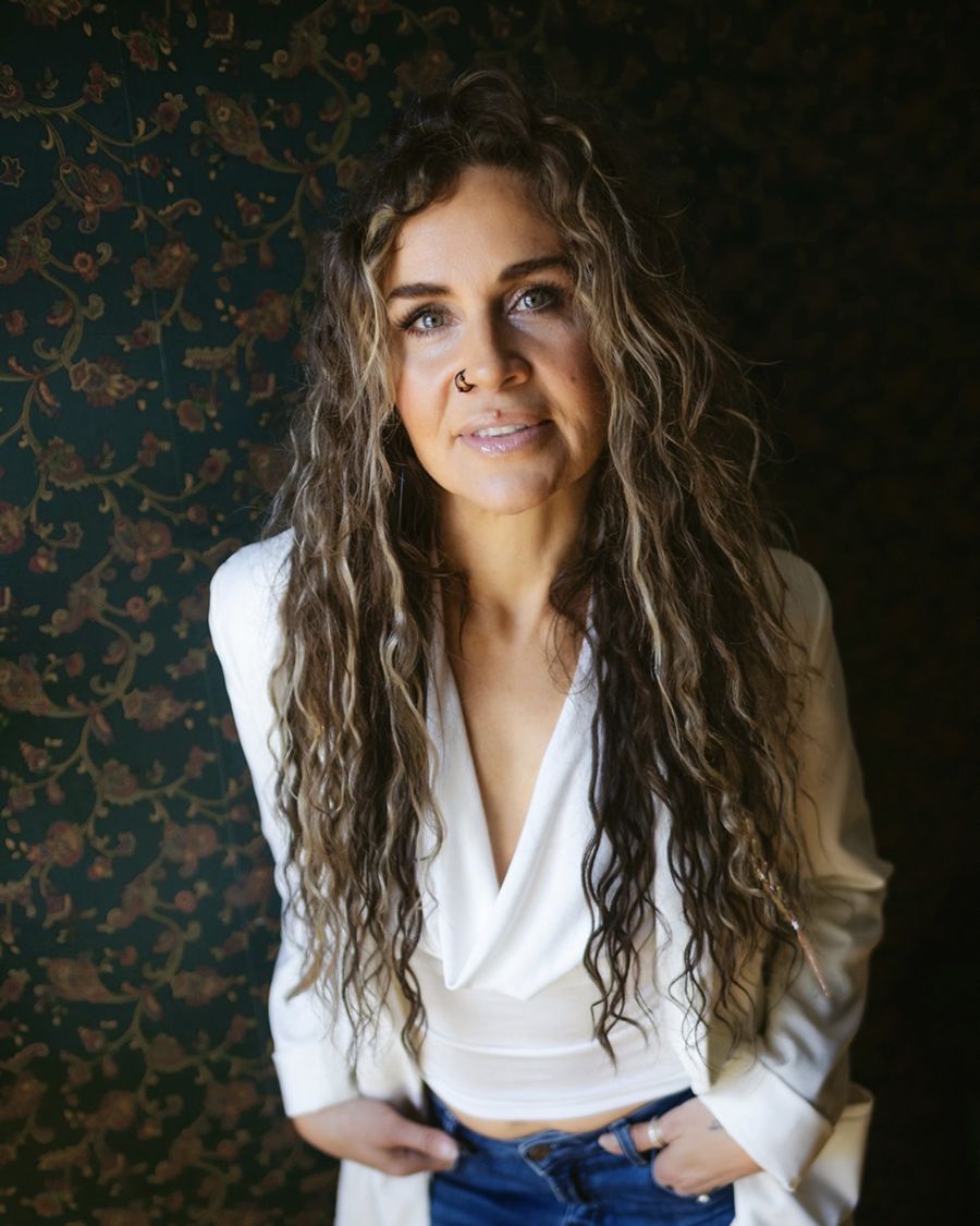 Julia Fisher in a white blazer against dark floral wallpaper